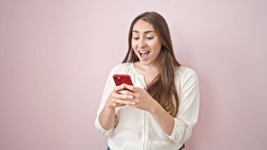 Akıllı telefon kullanan genç, güzel İspanyol kadın izole pembe arka planda gülümsüyor.