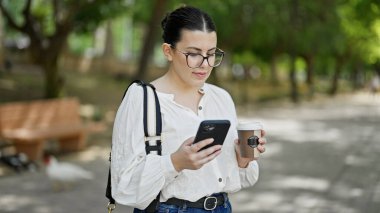 Genç ve güzel İspanyol kadın akıllı telefon kullanıyor. Parkta kahve içiyor.