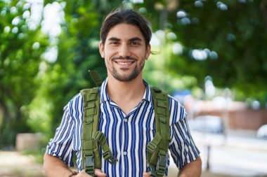 Genç İspanyol turist parkta sırt çantası takarak gülümsüyor.