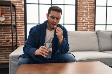 Genç İspanyol adam evdeki kanepede oturup hap alıyor.