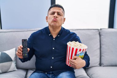 Latin asıllı genç adam patlamış mısır yiyor televizyon kumandasını kullanarak kameraya bakıyor öpücük yolluyor ve çok seksi oluyor. aşk ifadesi. 