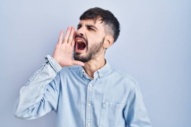 Mavi arka planda sakallı, ağzı açık bağırıp çağıran genç İspanyol bir adam. iletişim konsepti. 