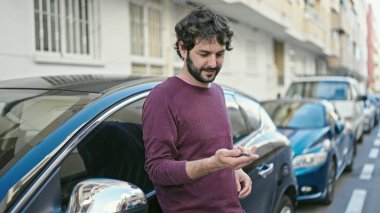 Young hispanic man smiling confident holding key of new car at street