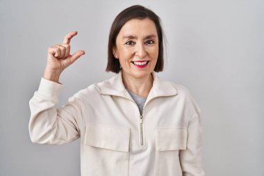 Middle age hispanic woman standing over isolated background smiling and confident gesturing with hand doing small size sign with fingers looking and the camera. measure concept. 