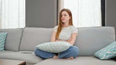 Kanepede oturan genç sarışın kadın ciddi bir yüz ve kollarını kavuşturdu.