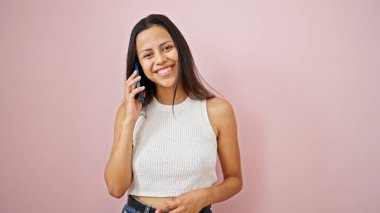 Genç, güzel, İspanyol bir kadın gülümsüyor. Akıllı telefondan kendine güvenen, izole pembe arka planda konuşan.