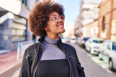 Afro-Amerikalı kadın gülümsüyor. Kendine güveniyor. Gökyüzüne bakıyor.