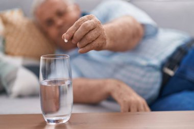 Middle age grey-haired man pouring pill on glass of water at home