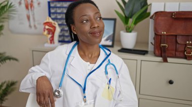 Afrikalı Amerikalı kadın doktor, klinikteki masada kendinden emin bir şekilde oturuyor.