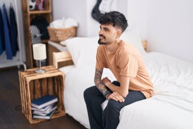 Young hispanic man smiling confident sitting on bed at bedroom