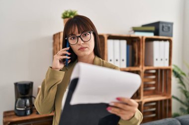 Genç, güzel İspanyol iş kadını. Ofiste akıllı telefon okuyarak konuşuyor.