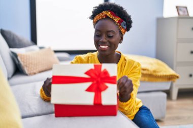 Young african american woman unboxing present package sitting on floor at home