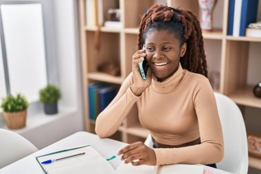 Afro-Amerikan bayan öğrenci akıllı telefondan konuşuyor evde masada oturuyor.