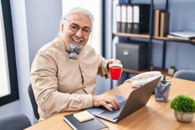Middle age grey-haired man business worker using laptop drinking coffee at office
