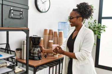 African american woman business worker holding jar and cup of coffee at office