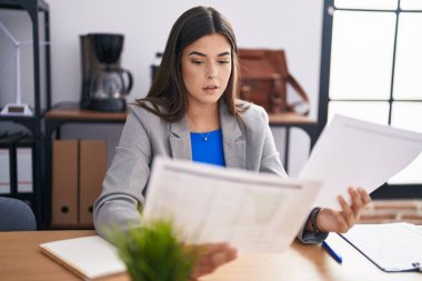 Young beautiful hispanic woman business worker reading document at office