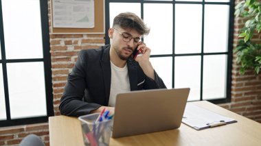 Genç Arap iş adamı ofiste bilgisayarla akıllı telefondan konuşuyor.