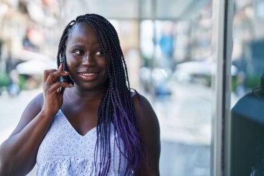 Afro-Amerikalı kadın gülümsüyor. Akıllı telefondan konuşuyor.