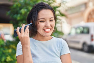 Young hispanic woman smiling confident listening audio message by the smartphone at street