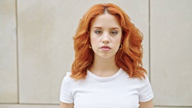 İzole edilmiş beyaz arka planda gevşek bir ifadeyle duran genç kızıl saçlı kadın.