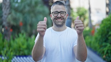 Gri saçlı, gülümseyen, kendine güveni tam. Parkta işaret veriyor.