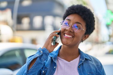 Afro-Amerikalı kadın gülümsüyor. Akıllı telefondan konuşuyor.