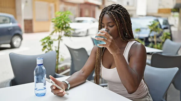 Αφροαμερικανή Γυναίκα Πίνοντας Ποτήρι Νερό Χρησιμοποιώντας Smartphone Στη Βεράντα Του — Φωτογραφία Αρχείου
