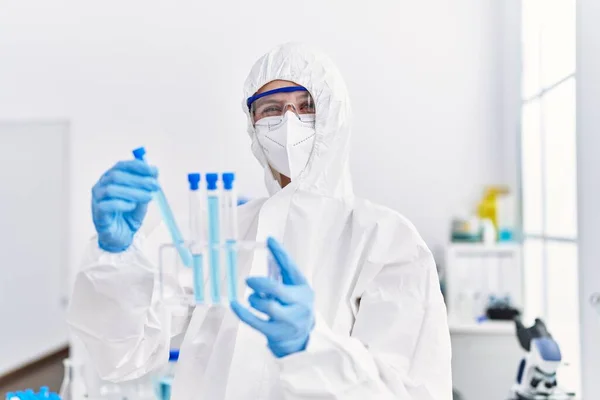 Young blonde woman scientist wearing security uniform holding test tubes at laboratory