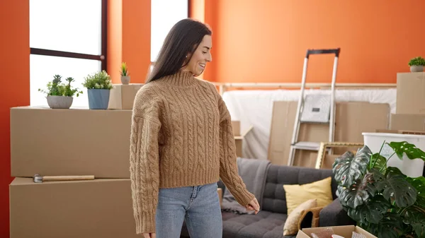 Genç, güzel, İspanyol bir kadın yeni evinde kendine gülerek duruyor.