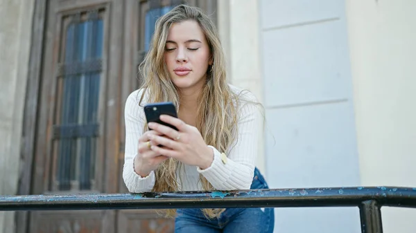 Młoda Blondynka Przy Użyciu Smartfona Poważnym Wyrazem Twarzy Ulicy — Zdjęcie stockowe