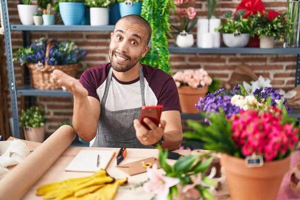 Çiçekçide sakallı İspanyol bir adam çalışıyor. Akıllı telefonuyla başarıyı kutluyor. Gülümsüyor ve elini kaldırıyor. 