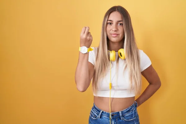 Młoda Blondynka Stojąca Nad Żółtym Tłem Słuchawkach Wykonująca Włoski Gest — Zdjęcie stockowe
