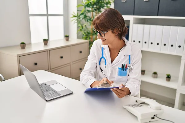 Stock image Young beautiful hispanic woman doctor using laptop writing medical report at clinic