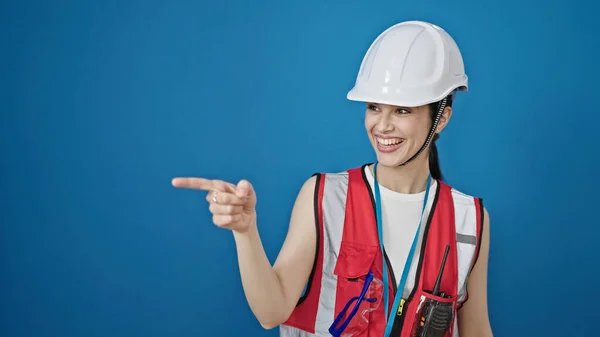 惊慌失措的女建筑工人面带微笑 自信地指着旁边孤零零的蓝色背景 — 图库照片