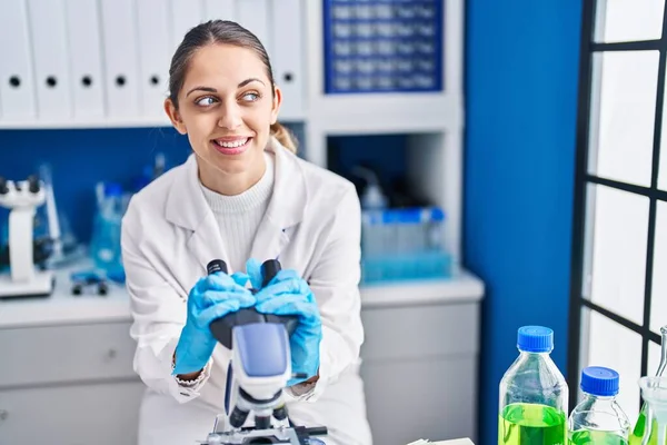 Young woman scientist smiling confident using microscope at laboratory