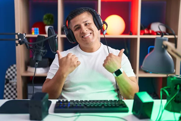 若いヒスパニック系の男性は 手で積極的なジェスチャーを行うビデオゲームの成功のサインを再生し 親指を笑顔と幸せ 陽気な表情と勝者のジェスチャー — ストック写真