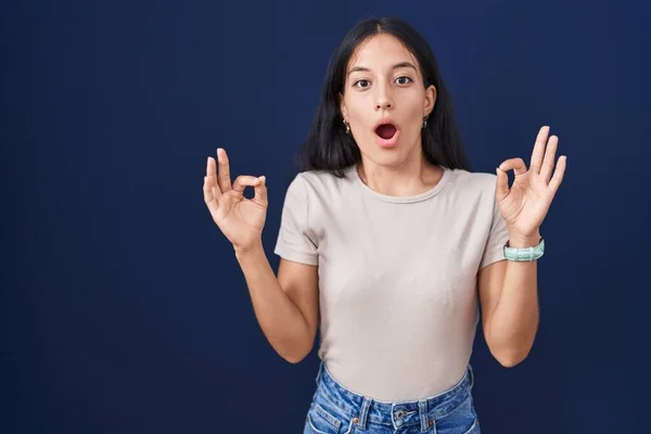 Tânără Hispanică Stând Deasupra Fundalului Albastru Surprinsă Șocată Făcând Simbolul — Fotografie, imagine de stoc