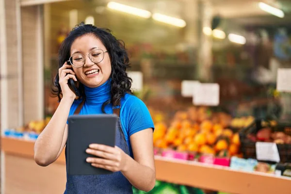 若い中国人女性従業員が果物店でタッチパッドを使用してスマートフォンで話しています — ストック写真