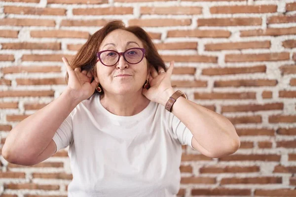 Mujer Mayor Con Gafas Pie Sobre Pared Ladrillos Tratando Escuchar —  Fotos de Stock