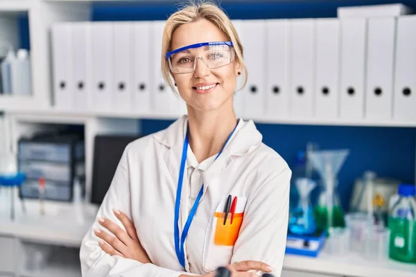 Young blonde woman scientist standing with arms crossed gesture at laboratory