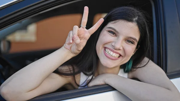 若いです美しいですヒスパニック女性座っています車の上で勝利ジェスチャーとともに指でストリート — ストック写真