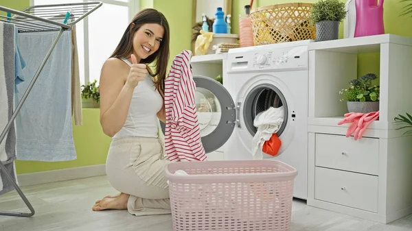 若い美しいヒスパニック女性は 洗濯室で笑顔で親指を上げる服を洗う — ストック写真