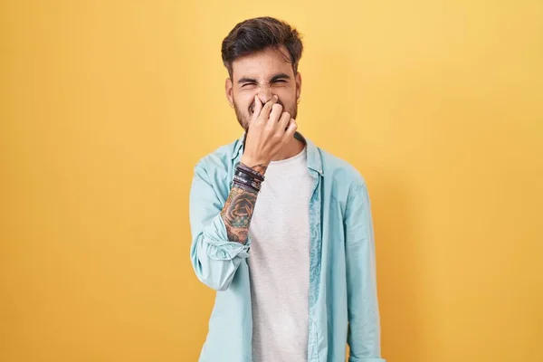 Young Hispanic Man Tattoos Standing Yellow Background Smelling Something Stinky — Fotografia de Stock