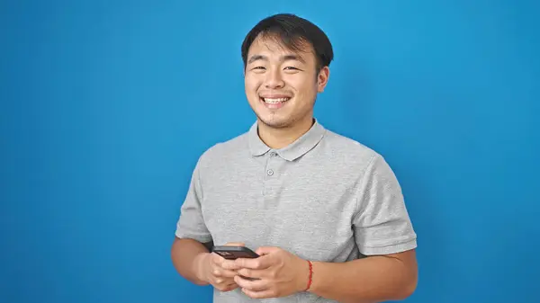 Usando Smartphone Sorrindo Sobre Fundo Azul Isolado — Fotografia de Stock