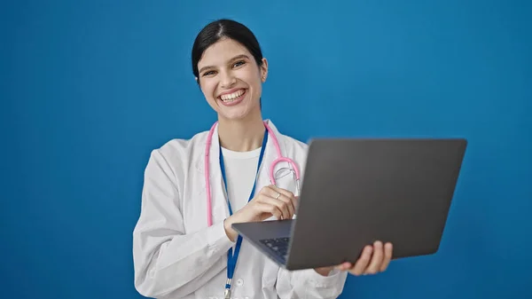 年轻美丽的惊慌失措的女医生用笔记本电脑站在孤立的蓝色背景上 — 图库照片