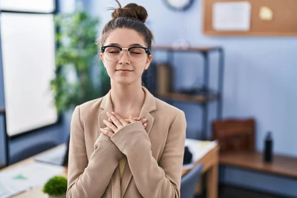 目を閉じたまま胸の上で手で微笑む眼鏡をかけたままオフィスで働く10代の少女と顔に感謝の表情 健康の概念 — ストック写真