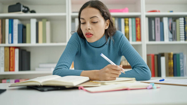 Young beautiful hispanic woman student writing on notebook at university classroom