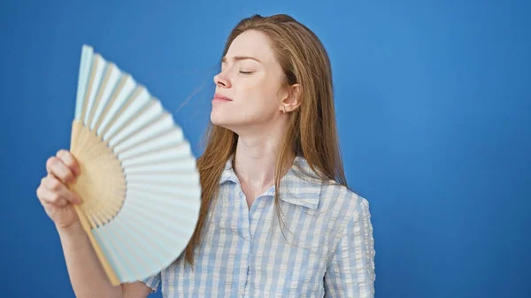 年轻的金发女人用手扇遭受热超过孤立的蓝色背景 — 图库照片
