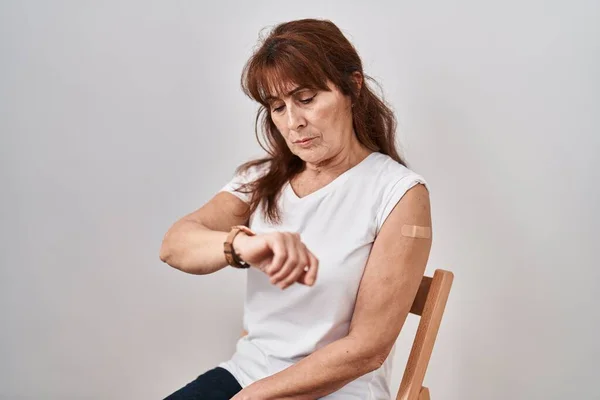 中年惊慌失措的女人拿着疫苗示臂 用创可贴检查腕表的时间 放松而自信 — 图库照片