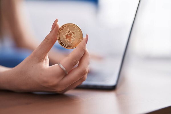 Young caucasian woman using laptop holding uniswap coin at home